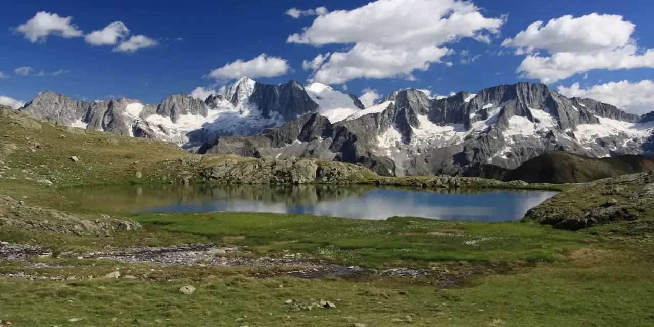 Laghi Val di Sole raggiungibili in auto: specchio d'acqua alpino con montagne innevate sullo sfondo e cielo azzurro con nuvole bianche.