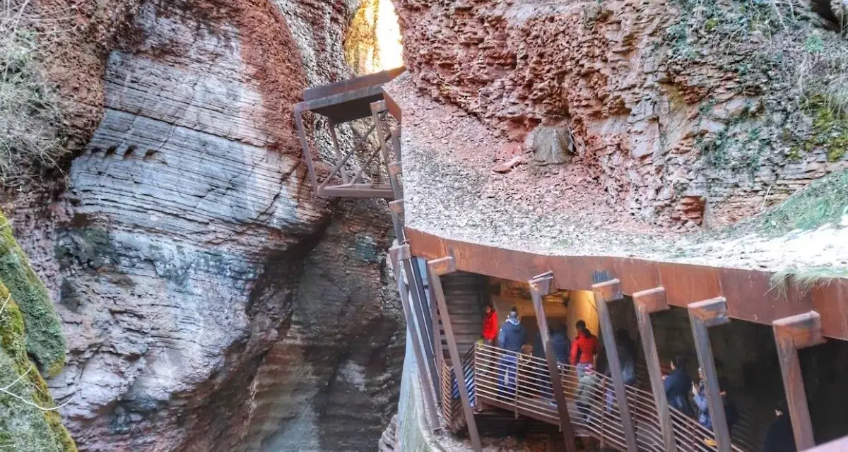 Persone percorrono una passerella metallica lungo le pareti rocciose di un canyon, vicino al Ponte dell'Orrido.