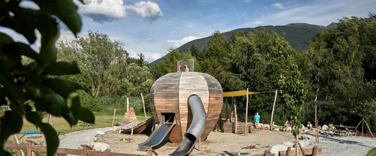 Un colorato parco giochi Trentino con una struttura a forma di sfera in legno, scivoli e bambini che giocano.
