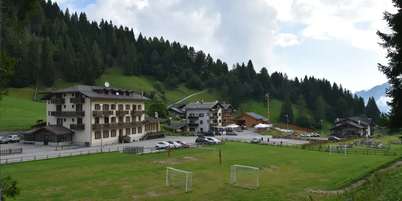 Edifici alpini e un campo da calcio con porte, immersi nel verde e circondati da boschi. La **passo Cereda altitudine** offre uno scenario incantevole.