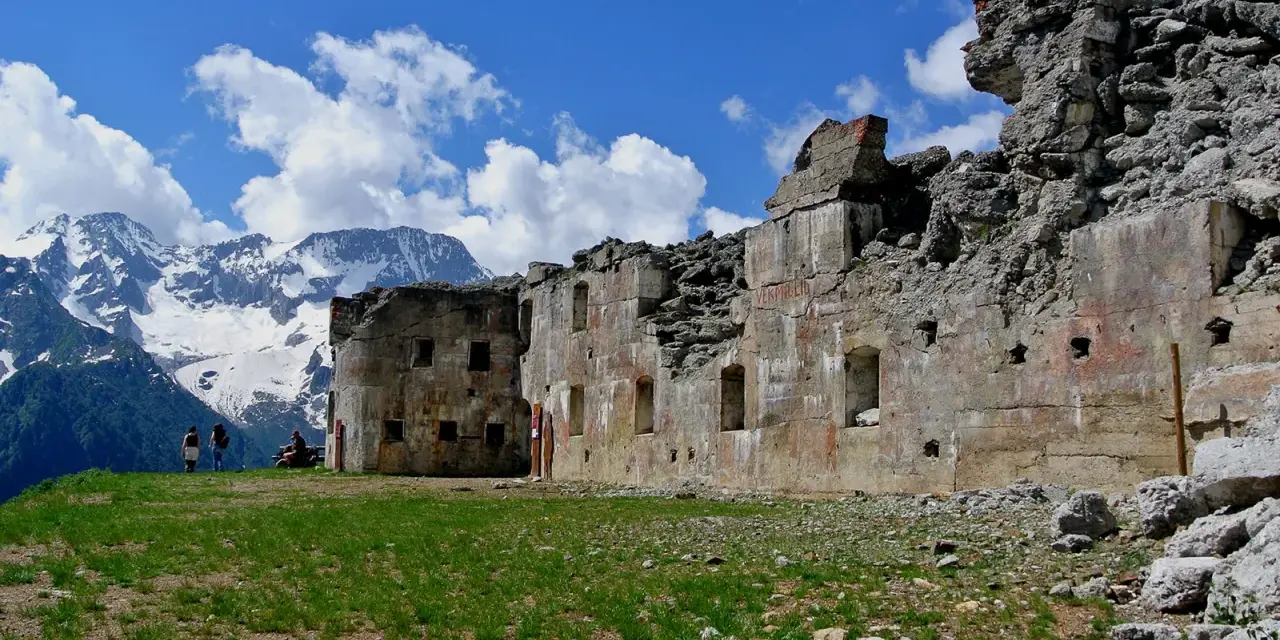 Rovine del forte Zaccarana, con montagne innevate sullo sfondo e cielo azzurro con nuvole bianche.