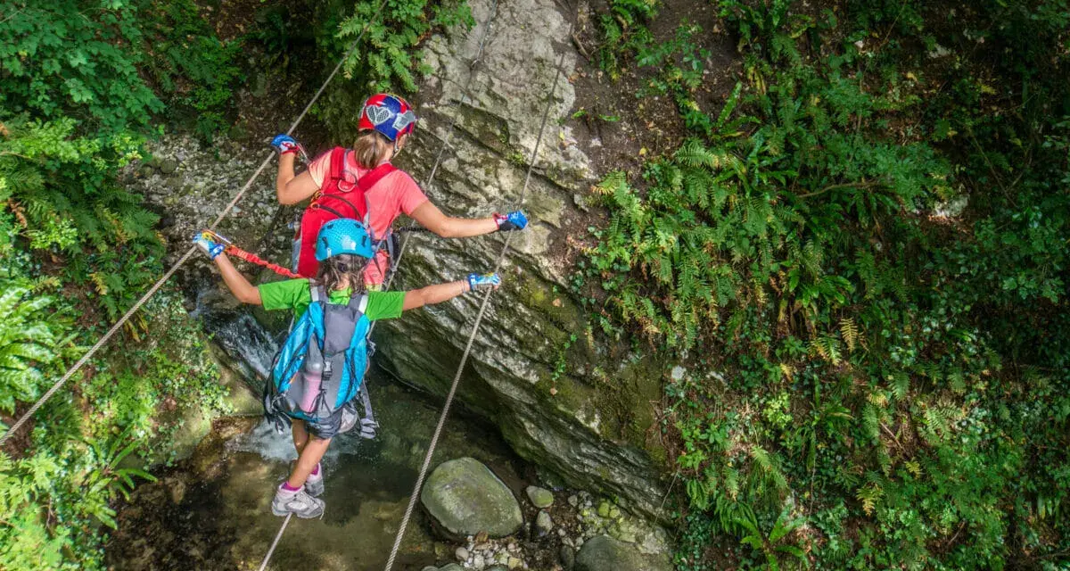 Bambini affrontano un emozionante percorso ponte tibetano tra rocce e vegetazione lussureggiante.
