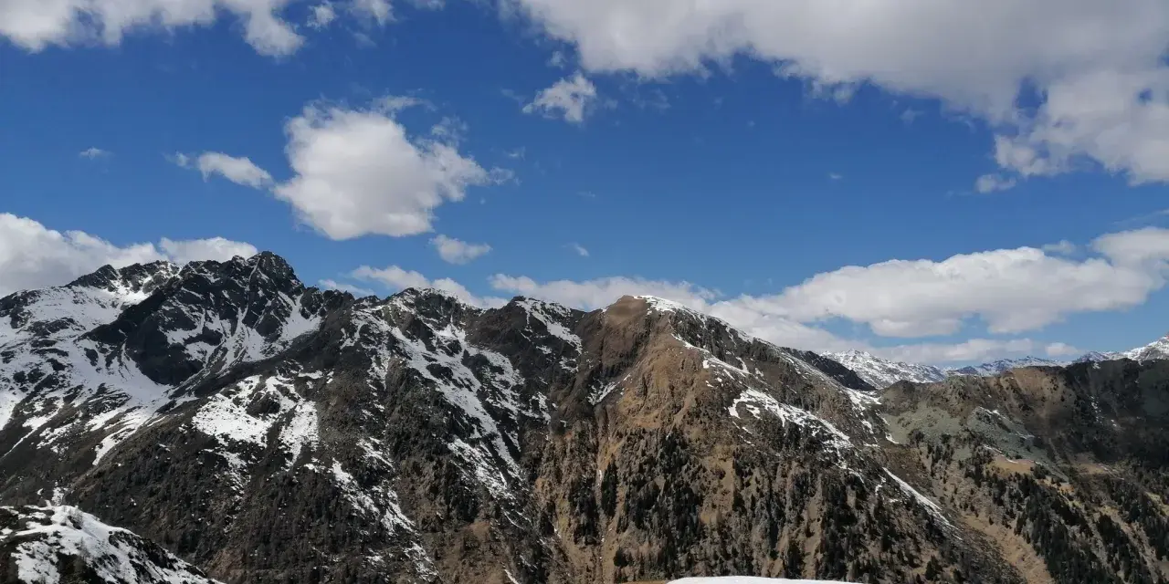 Cimon di Bolentina, un maestoso panorama montuoso con cime innevate e un cielo azzurro punteggiato di nuvole bianche.