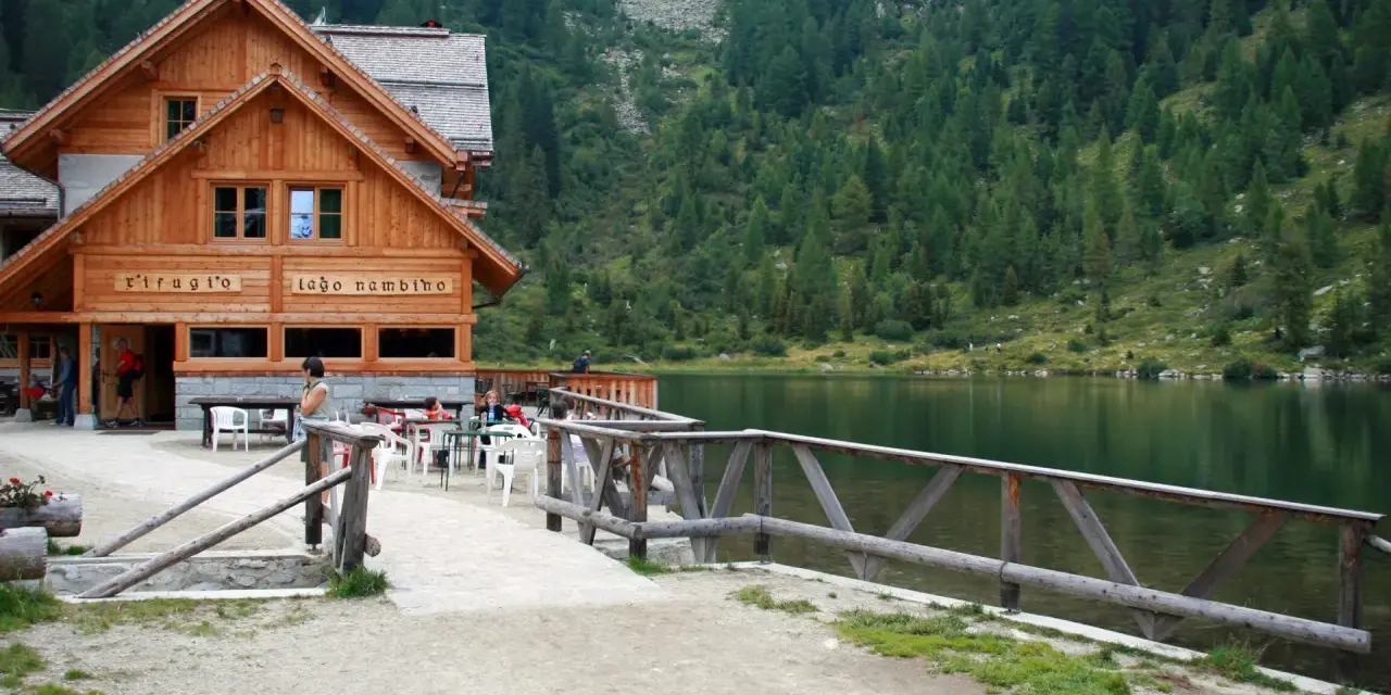 Rifugio sul lago nambino, con tavoli all'aperto e un bosco di conifere sullo sfondo.