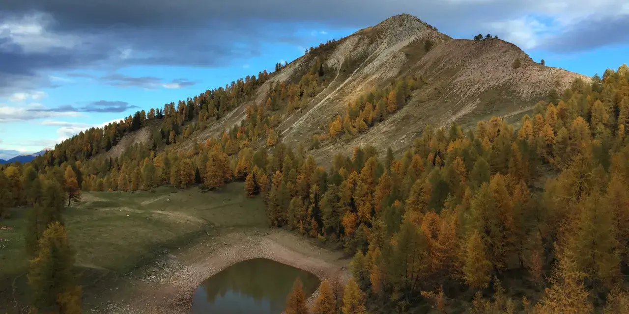 Autunno dorato sul lago delle salare, con larici color ocra che abbracciano la montagna e riflettono il cielo nuvoloso.