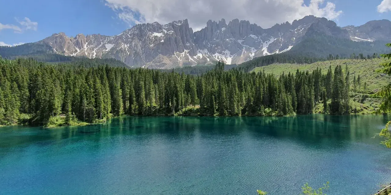 Laghi alpini in Val di Fassa, con acque cristalline che riflettono la foresta di abeti e le maestose cime dolomitiche innevate.
