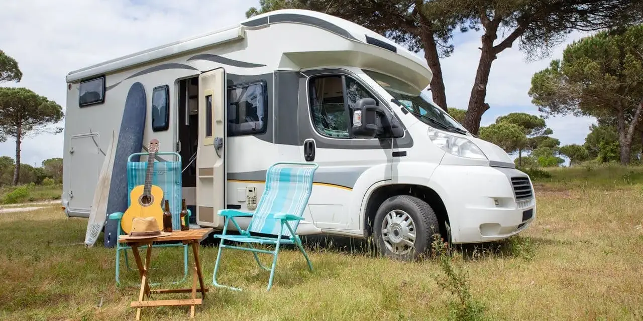 Un camper pronto per un tour in Trentino, con chitarra, cappello e sedie da campeggio in un prato verde.