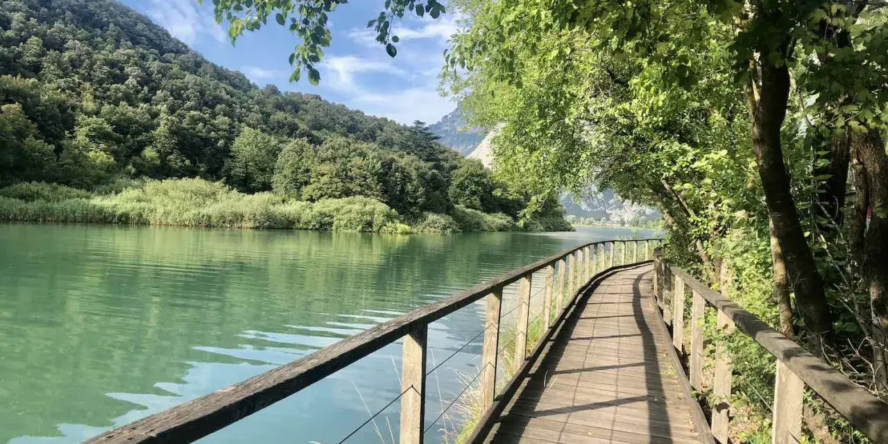 Sentiero in legno lungo il lago di Toblino, con montagne verdi sullo sfondo. Ideale per scoprire come arrivare.