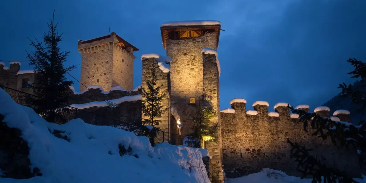 Castello innevato illuminato di notte, con alberi di Natale e luci che ricordano i mercatini di Natale di Ossana.