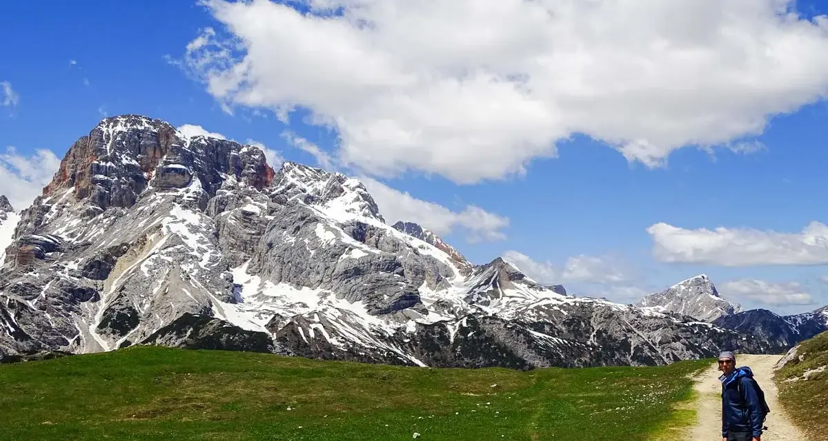 Un escursionista si ferma su un sentiero di montagna, con imponenti vette innevate sullo sfondo. Perfetti percorsi per camminare.