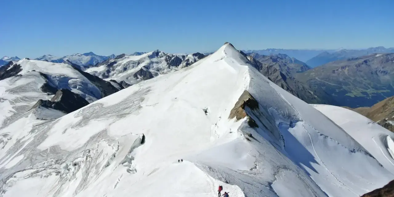 Alpinisti in cammino sulla cresta innevata del ghiacciaio Cevedale, con vette maestose sullo sfondo.