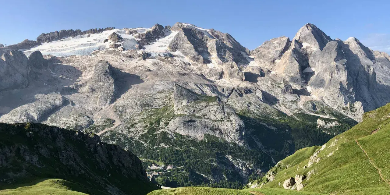 Vette innevate del Viel del Pan si stagliano maestose su un paesaggio alpino verdeggiante, con un piccolo borgo incastonato tra i boschi.