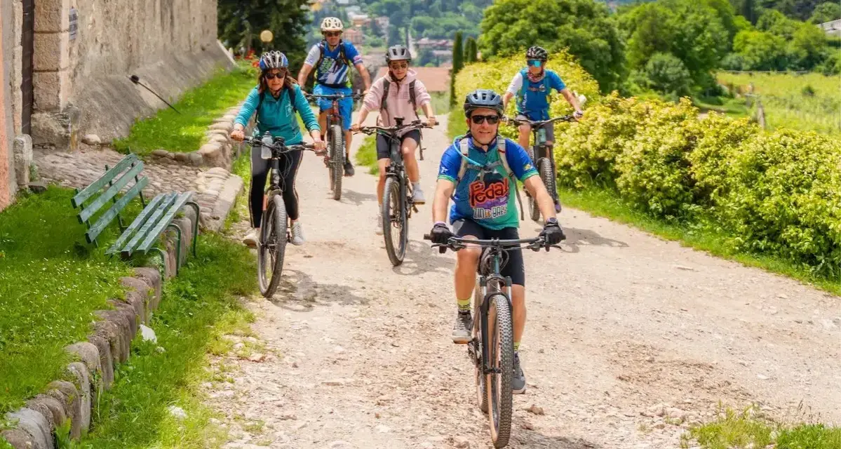 Gruppo di ciclisti su sentiero sterrato, godendosi gli eventi Trentino in un paesaggio verdeggiante.