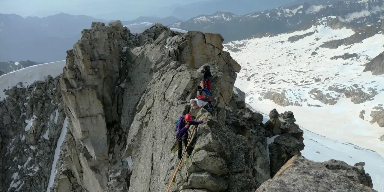 Alpinisti in cordata affrontano un crinale roccioso innevato, con la **cima Presanella** sullo sfondo.