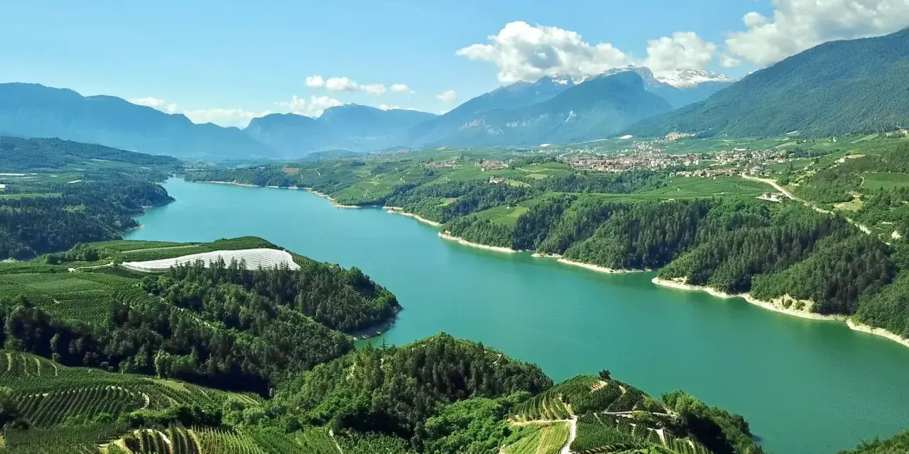 Panoramica mozzafiato del lago di Santa Giustina, circondato da verdi colline coltivate e montagne imponenti.