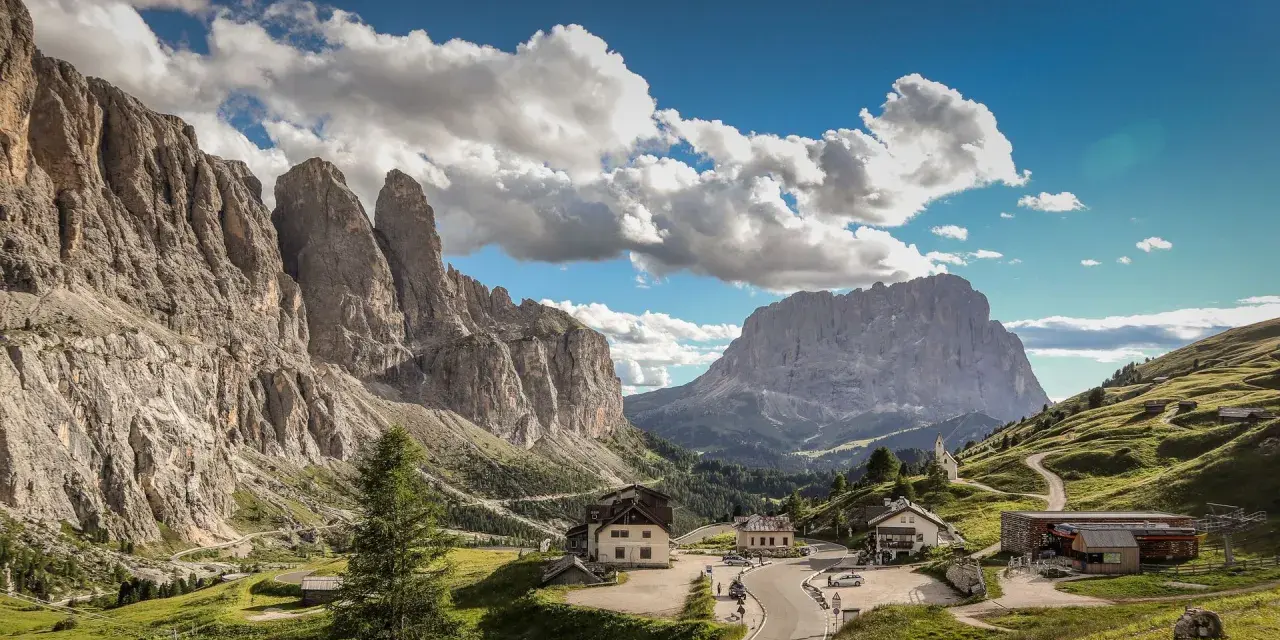 Panorami mozzafiato al Passo Gardena, con imponenti vette rocciose e un'altitudine che toglie il fiato. Case e strade si snodano tra i verdi pendii.