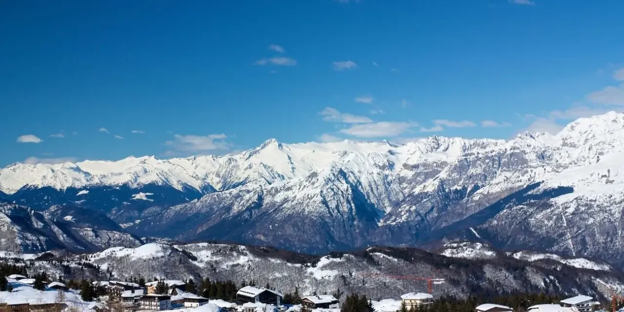 Paesaggio invernale con case innevate e montagne maestose sullo sfondo, un incantevole scenario al Passo Bondone.