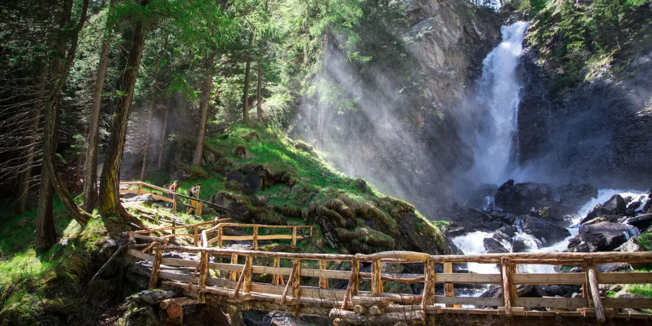 Sentiero in legno conduce alle maestose cascate Val di Sole, immerse in un bosco rigoglioso.