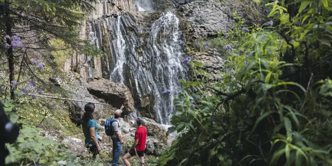 Escursionisti ammirano le spettacolari cascate schiavaneis, immerse nel verde e circondate da rocce basaltiche.