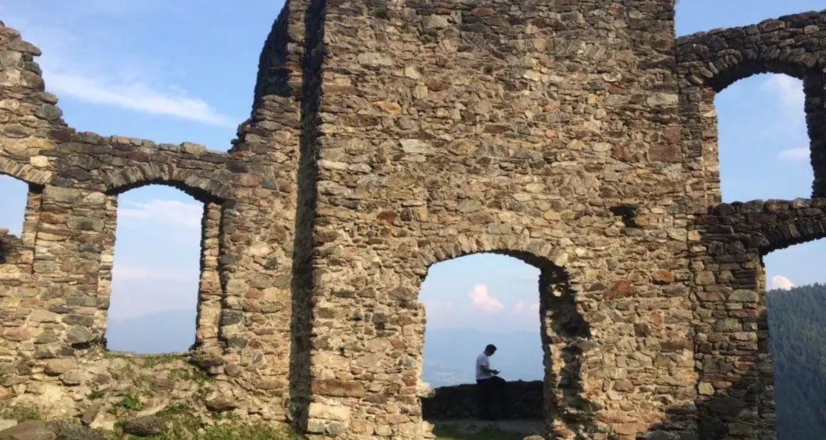 Rovine del castello di Altaguardia, con un uomo seduto che guarda il panorama.