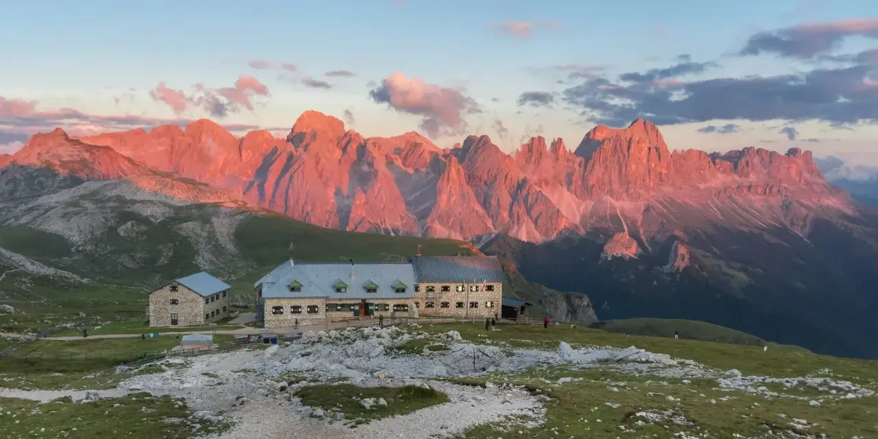 Rifugio sul **Monte Catinaccio** illuminato dal tramonto, con le vette rocciose che si tingono di rosa.