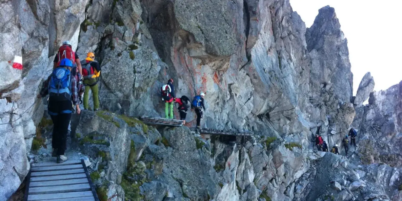 Escursionisti su un sentiero attrezzato, un'avventura di trekking in Adamello tra rocce e passerelle di legno.