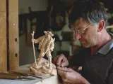 Maestro intaglia un pastore con bastone, un esempio di artigianato legno trentino.