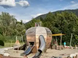 Un colorato parco giochi Trentino con una struttura a forma di sfera in legno, scivoli e bambini che giocano.