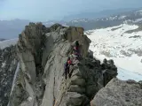 Alpinisti in cordata affrontano un crinale roccioso innevato, con la **cima Presanella** sullo sfondo.