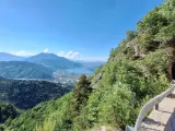 Vista panoramica dal Monte Vezzena con lago azzurro e montagne sullo sfondo. Strada con galleria scavata nella roccia.