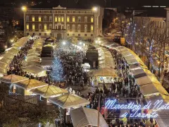 Un affollato Mercatino di Natale a Trento, con bancarelle illuminate, un albero scintillante e gente che passeggia tra le luci festive.