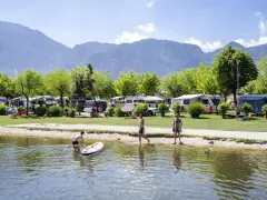 Giovani si godono il lago di Levico spiaggia, con campeggio e montagne sullo sfondo.