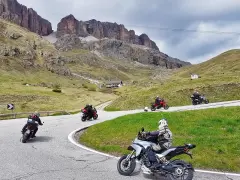 Motociclisti affrontano tornanti sui **Dolomiti passi**, con imponenti vette sullo sfondo.