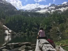 Bambina seduta su un tronco guarda il lago di Barco, circondato da montagne innevate e foreste di conifere.