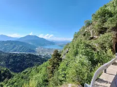 Vista panoramica dal Monte Vezzena con lago azzurro e montagne sullo sfondo. Strada con galleria scavata nella roccia.