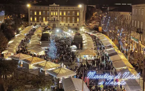Un affollato Mercatino di Natale a Trento, con bancarelle illuminate, un albero scintillante e gente che passeggia tra le luci festive.