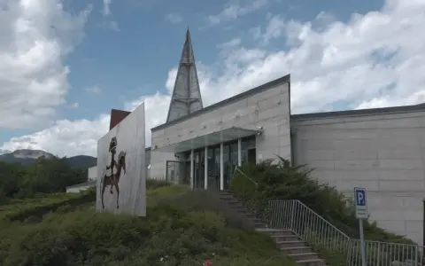Il museo retico, con la sua architettura moderna e un'installazione artistica di un guerriero a cavallo, si erge sotto un cielo nuvoloso.