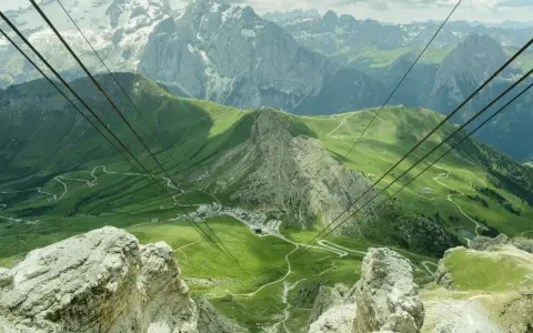 Vista mozzafiato da Canazei al Passo Sella, con funivia che attraversa verdi pendii e imponenti vette dolomitiche.