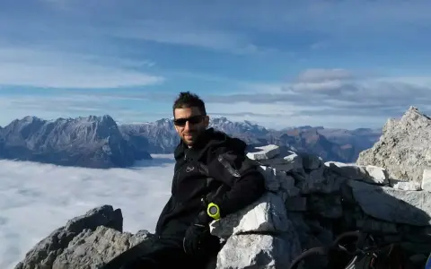 Uomo in vetta con abbigliamento tecnico, ideale per capire come vestirsi in montagna a settembre. Paesaggio alpino mozzafiato.