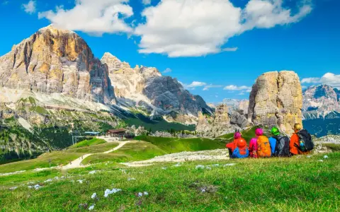 Quattro escursionisti ammirano le maestose Dolomiti Trentino Alto Adige, con cime imponenti e un cielo azzurro.