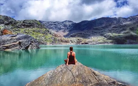 Donna seduta su una roccia ammira il **lago del Carest** con le montagne sullo sfondo.