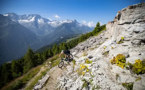 Ciclista in discesa su sentiero roccioso, con montagne innevate sullo sfondo, durante il giro dei forti tonale.