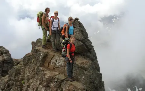 Quattro escursionisti con zaini si fermano sulla cima rocciosa di Cima Sternai, circondati da nuvole e nebbia.