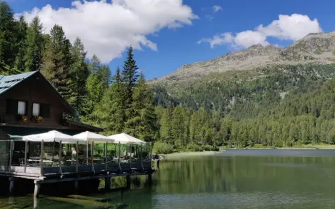 Rifugio in legno con tavoli all'aperto sul lago, circondato da boschi e montagne. Un luogo incantevole per scoprire cosa vedere a Pellizzano.