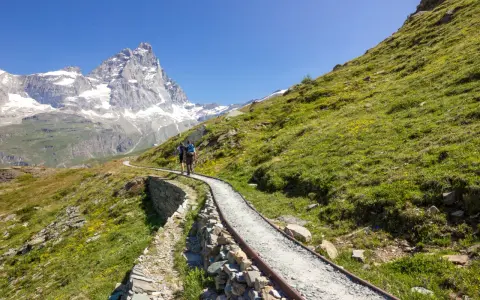 Due escursionisti affrontano un sentiero panoramico, con il Cervino innevato sullo sfondo, durante un **trekking due giorni Dolomiti**.