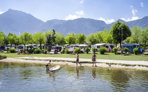 Giovani si godono il lago di Levico spiaggia, con campeggio e montagne sullo sfondo.