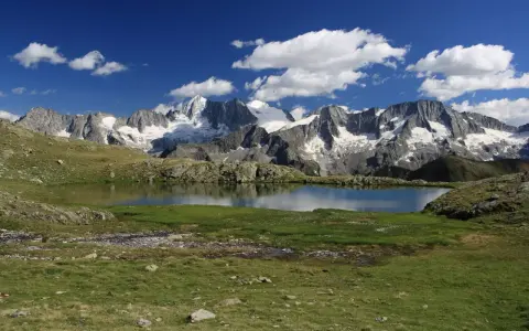 Laghi Val di Sole raggiungibili in auto: specchio d'acqua alpino con montagne innevate sullo sfondo e cielo azzurro con nuvole bianche.