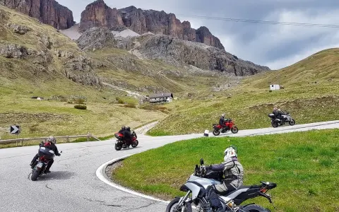 Motociclisti affrontano tornanti sui **Dolomiti passi**, con imponenti vette sullo sfondo.