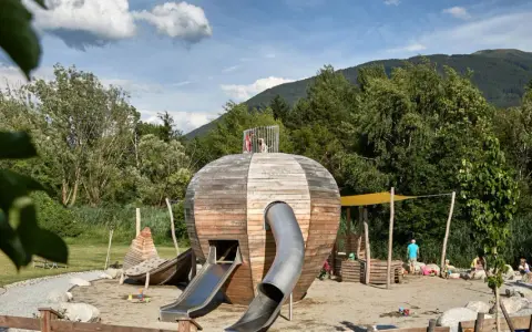 Un colorato parco giochi Trentino con una struttura a forma di sfera in legno, scivoli e bambini che giocano.