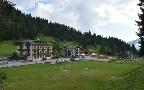 Edifici alpini e un campo da calcio con porte, immersi nel verde e circondati da boschi. La **passo Cereda altitudine** offre uno scenario incantevole.